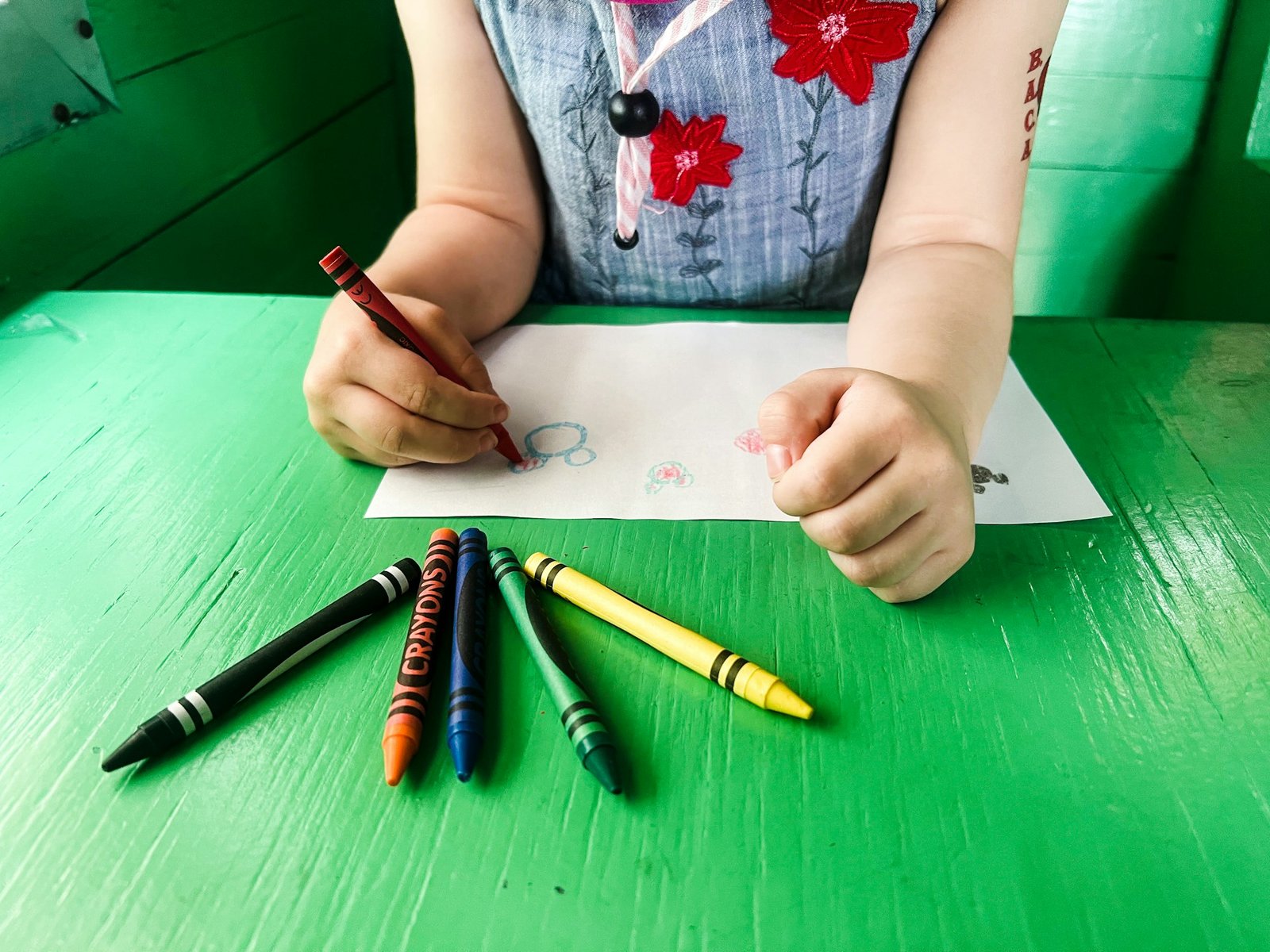 Toddler coloring with a red crayon at a green table