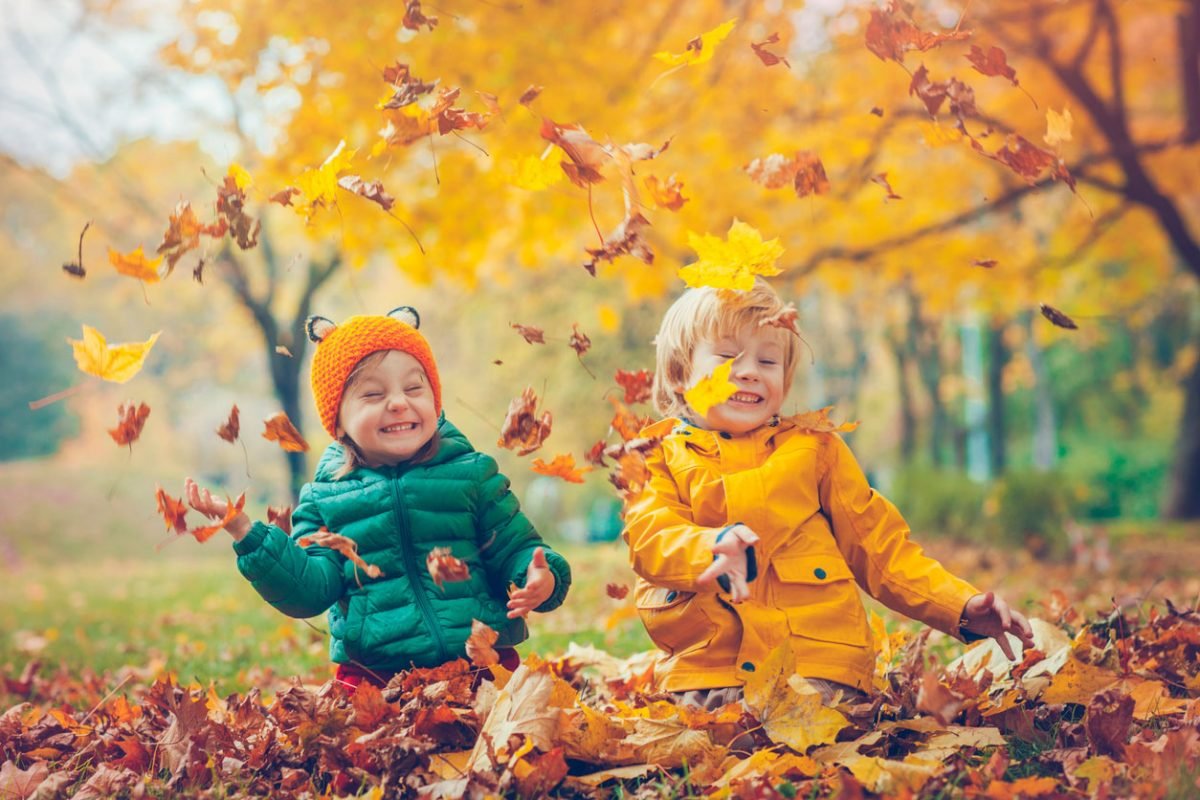 Two happy children throwing autumn leaves in the air at a park