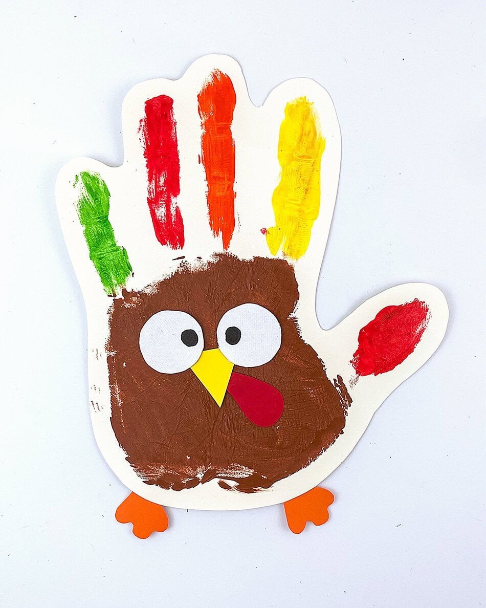 Handprint turkey craft with painted finger feathers, googly eyes, and a paper beak on white paper